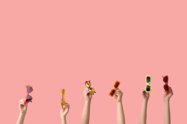 Female hands with different stylish sunglasses on pink background