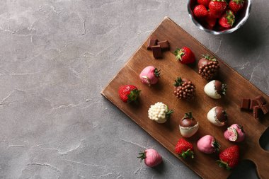 Çikolata kaplı çilekli ahşap tahta tahta ve gri arka planda bir kase taze çilek.