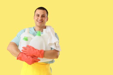 Sarı arka planda çamaşır deterjanı şişeleri olan genç bir adam.