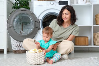 Küçük şirin bebek, annesine banyoda çamaşır yıkamada yardım ediyor.