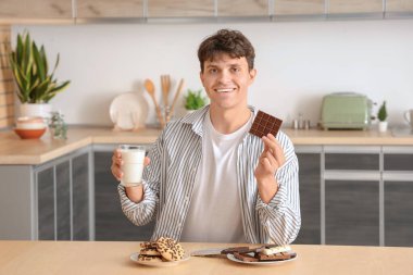 Bir tabak çikolatalı, lezzetli kurabiyeli ve mutfaktaki masada bir bardak sütü olan yakışıklı genç adam.