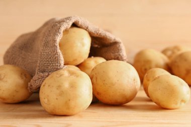 Tahta arka planda çiğ patatesli çuval.