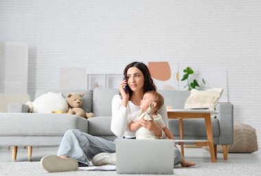 Evde doğum izninde cep telefonuyla konuşurken dizüstü bilgisayarla çalışan sevimli küçük bebek ve genç anne.