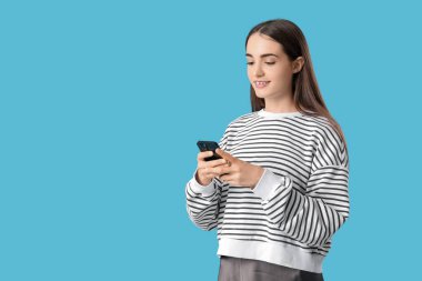 Mavi arka planda cep telefonu olan güzel, genç bir kadının portresi.