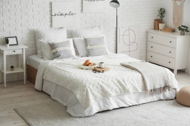 Yatak odasının içinde lamba, kahvaltı ve yatağın üstünde kitaplar var.