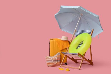 Güverte sandalyesi, plaj şemsiyesi, bavul, şapka, çanta, parmak arası terlik ve pembe arka planda şişme yüzük.