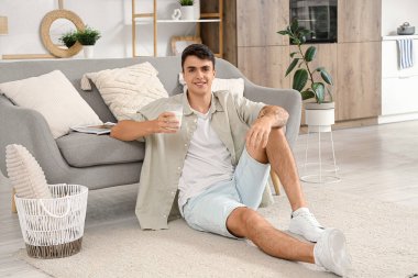 Evde yerde oturan bir bardak sütle yakışıklı genç adam.