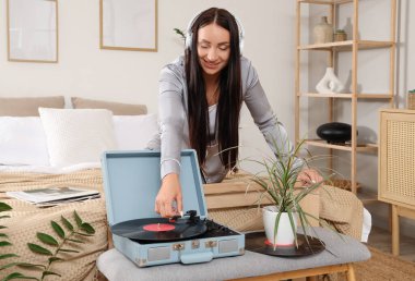Yatak odasında müzik çalar kullanan kulaklıklı genç bir kadın.