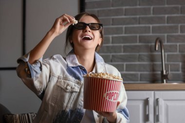 Genç bir kadın elinde patlamış mısırla mutfakta film izliyor.