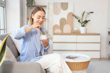 Chia tohumu pudingi olan genç bir kadın evdeki koltukta oturuyor.