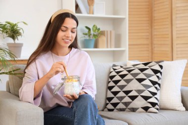 Chia tohumu pudingi olan genç bir kadın evdeki koltukta oturuyor.