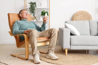 Cep telefonlu yaşlı adam evdeki koltukta oturuyor.