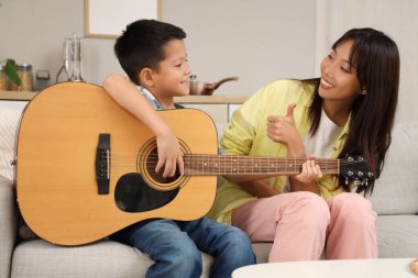 Küçük çocuk evde annesiyle gitar çalıyor.