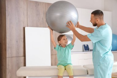 Rehabilitasyon merkezinde kanepede spor ve fizyoterapist eğitimi alan küçük bir kız.