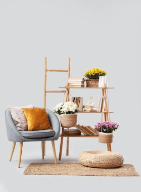 Gri koltuk, merdiven, dekorlu raf ünitesi ve beyaz arka planda kasımpatı çiçekleri