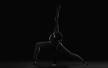Siyah arka planda yoga yapan genç bir kadının silueti.
