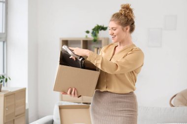 Evde yeni çantasıyla paket kutusunu açan genç bir kadın.