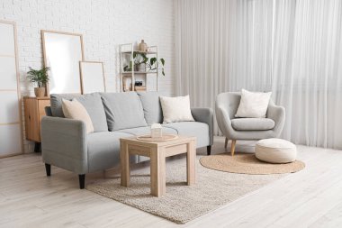 Konforlu kanepe, koltuk, sehpa ve oturma odasındaki beyaz tuğla duvarın yanındaki boş posterler.