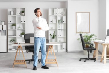 Genç adam ofiste cep telefonuyla konuşuyor.