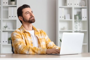 Bilgisayarlı yakışıklı adam masadaki masaya doğru bakıyor.
