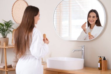 Banyoda aynanın yanında serum uygulayan genç bir kadın.