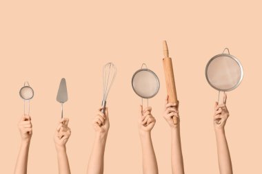 Kadın eli çırpılmış süzgeçler, pasta spatulası ve bej arka planda merdane.