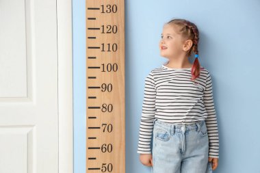 Evdeki mavi duvarın yanında küçük bir kız stadyum ölçer ile boy ölçüyordu.
