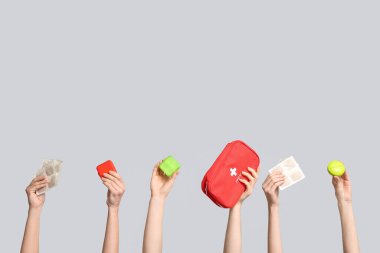 Hardal alçılı kadın elleri, ilaç kutuları ve gri arka planda ilk yardım çantası.