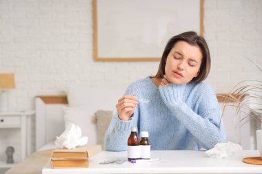 Yatak odasındaki masada öksürük şurubu alan hasta genç bir kadın.
