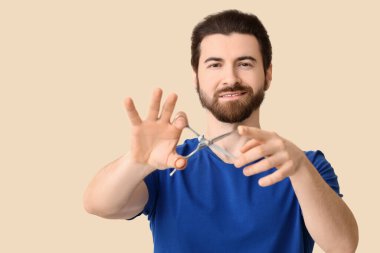 Bej arka planda makasla sakallı genç bir adam.