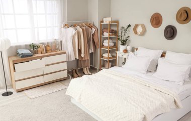 Konforlu yatak, çekmeceler ve modern yatak odasındaki giysili askılar.