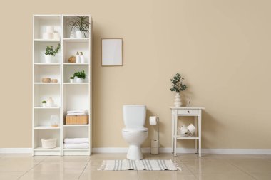 Raflama ünitesi, klozet ve tuvalet kağıdıyla dolu masa. Banyoda bej duvarın yanında.