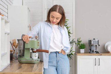 Güzel genç bir kadın, mutfakta kahve makinesiyle kahve yapıyor.