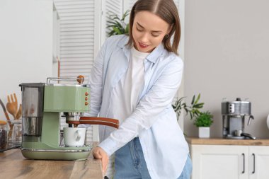 Güzel genç bir kadın, mutfakta kahve makinesiyle kahve yapıyor.