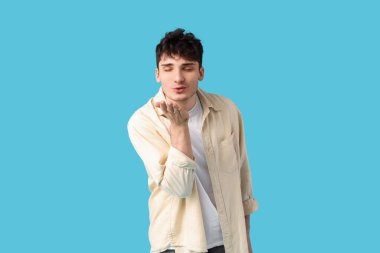 Yakışıklı genç adam mavi arka planda öpüşüyor.