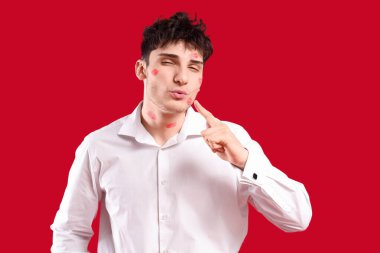 Yüzünde dudak izleri olan yakışıklı genç adam kırmızı arka planda öpüşüyor.