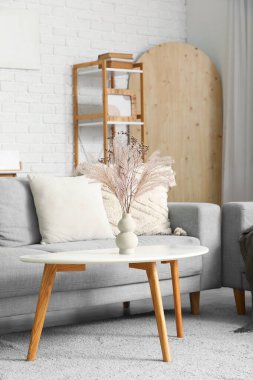 Oturma odasındaki gri kanepenin yanındaki masada kuru kamışlı vazo.