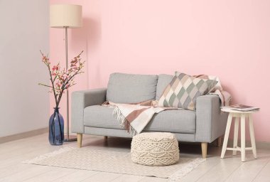 Konforlu kanepe, sehpa ve pembe duvarın yanında çiçek açan ağaç dalları.