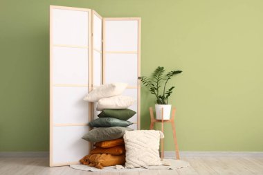 Katlanan ekran, çiçek ve yastıklar yeşil duvarın yanında.