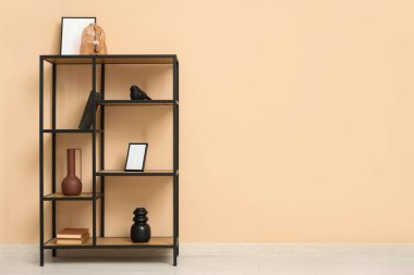 Raflarda kitaplar, vazolar ve çerçevelerle bej duvarın yanında.