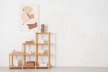 Odasında beyaz tuğla duvarın yanında kitap ve dekor olan ahşap raf ünitesi.