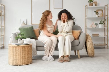 Evdeki kanepede üzgün Afrikalı-Amerikalı arkadaşını destekleyen güzel bir genç kadın.