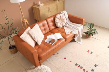 Oturma odasının içinde kahverengi deri kanepe, klozet ve çiçek var.