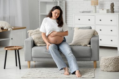 Evdeki kanepede diz ağrısı çeken hamile bir kadın.