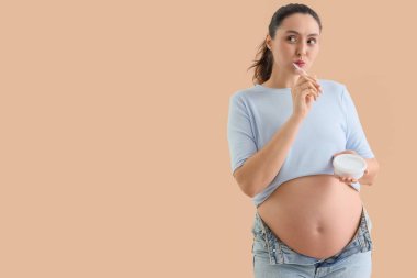 Bej arka planda diş fırçalayan hamile bir kadın.