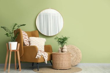 Oturma odasındaki yeşil duvarda asılı duran zarif yuvarlak ayna.