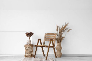 Sandalye, otlar ve çiçekler odadaki beyaz duvarın yanındaki vazoda kahve masasının üzerinde.