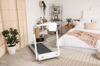 Koşu bandı, raf üniteleri ve bitkilerle aydınlık yatak odasının içinde.