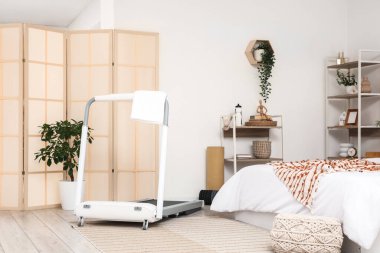 Koşu bandı, raf üniteleri ve bitkilerle aydınlık yatak odasının içinde.