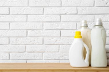 Beyaz tuğla duvarın yanında çamaşır deterjanı şişeleri olan ahşap bir bank.